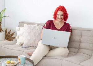 Lachende auf einer Couch sitzende Vanessa tippt auf einem Laptop - Vanessa Bause Rock your Finances